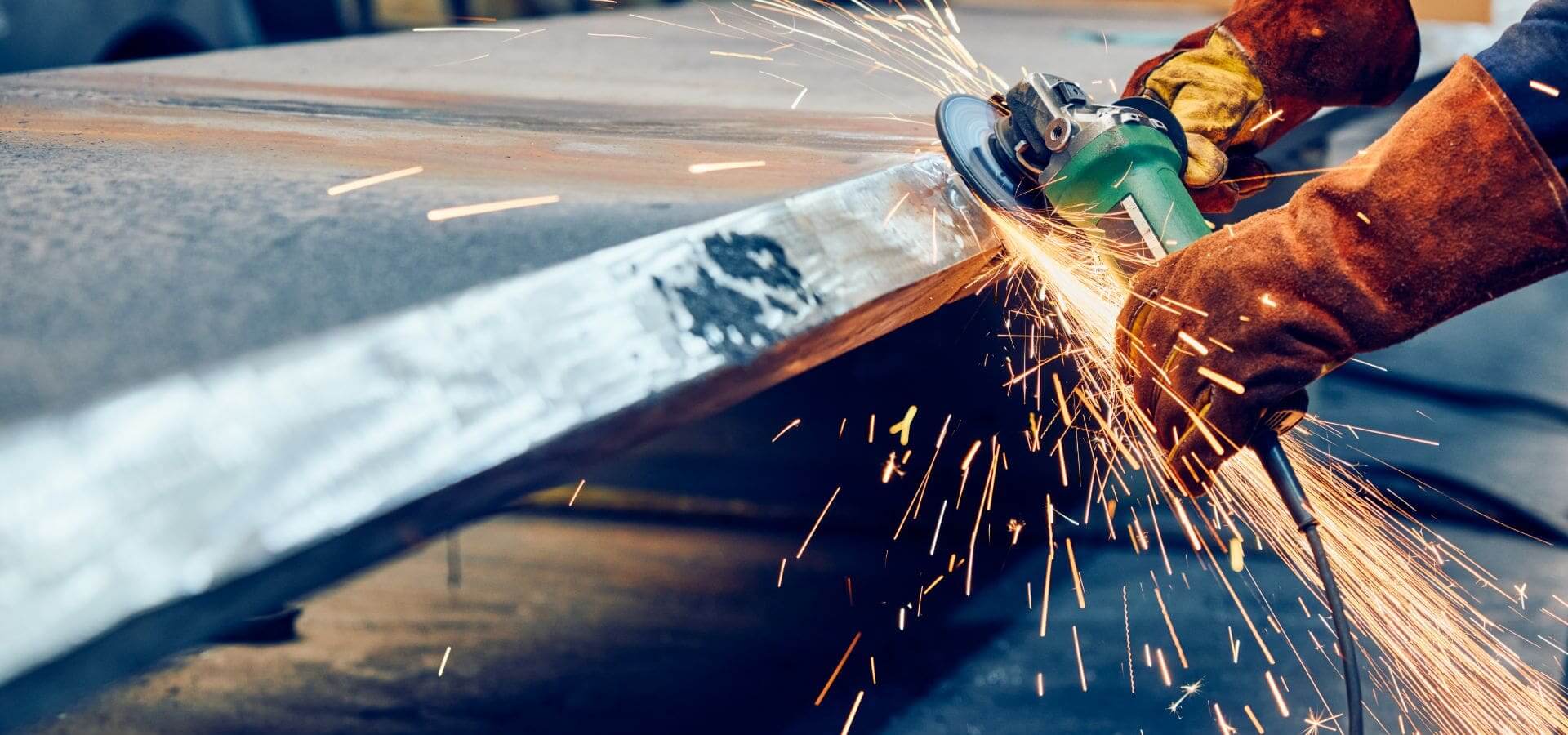 Worker grinding metal, sparks flying, protective gloves.