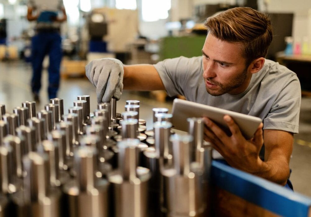 Man inspecting metal parts in factory setting.